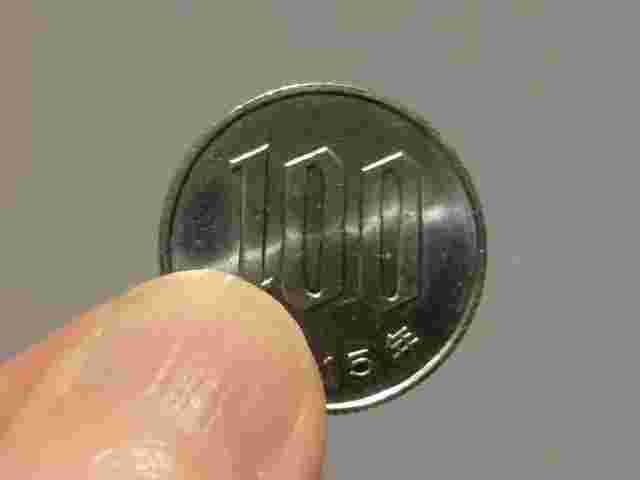 指でつまんだ100円玉硬貨