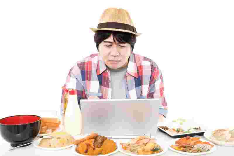 高カロリーな食品に囲まれPCを使って調べものをする男性
