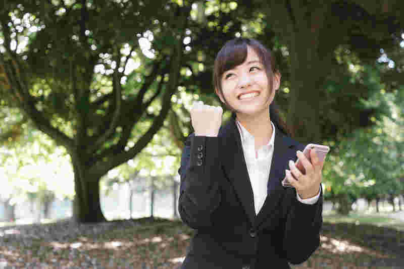 公園でスマホをもってガッツポーズする女性