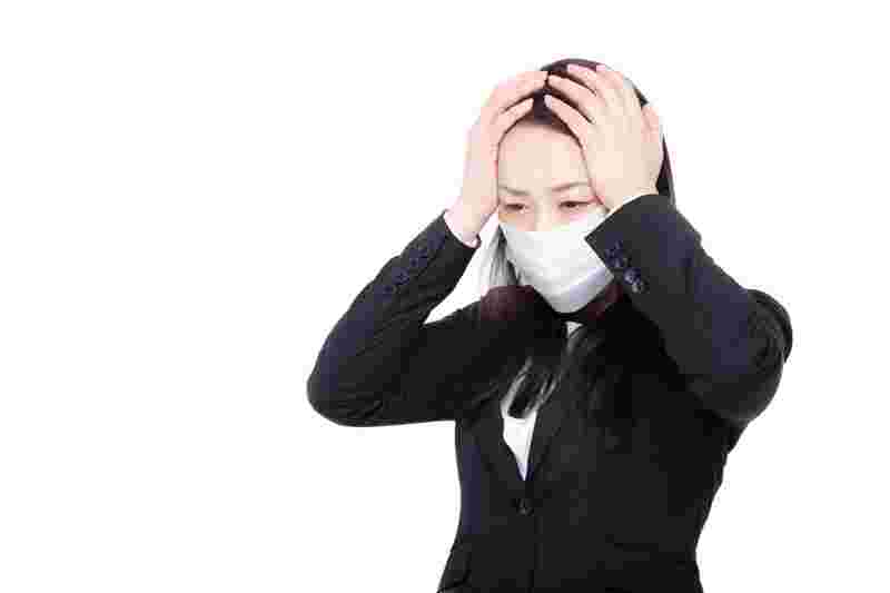 マスクをして両手を頭にあてて辛そうな女性