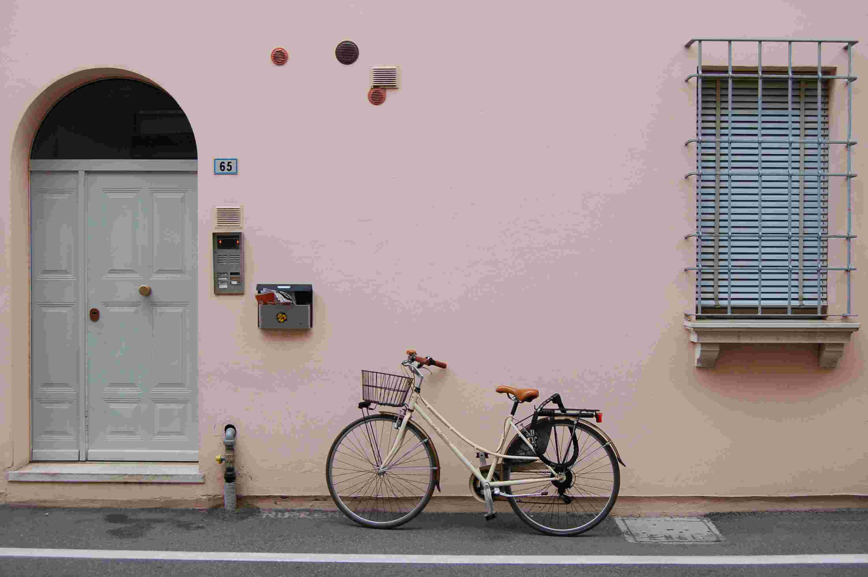 ピンクの塗られた壁の建物に駐車されている白い通勤自転車