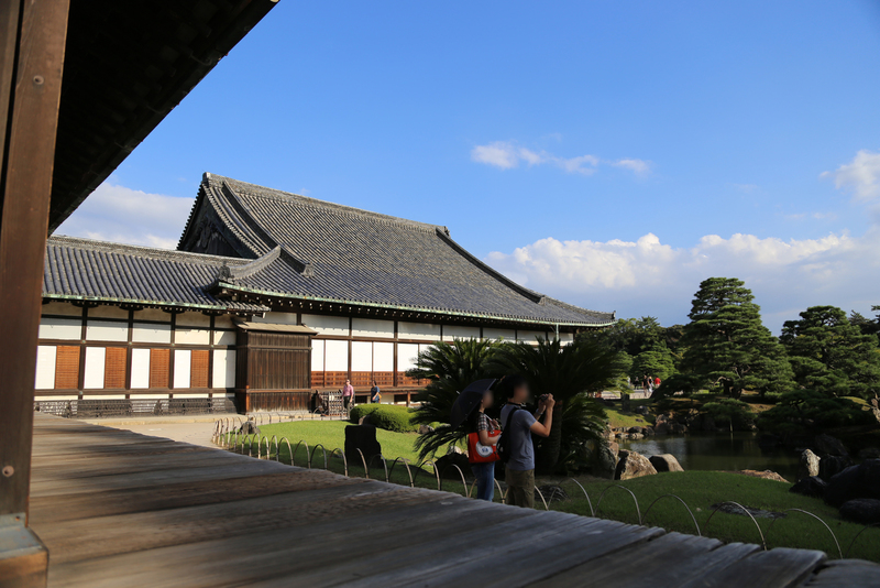 【二条城二の丸御殿の黒書院・蘇鉄の間・大広間】<p>二条城二の丸御殿の黒書院の廊下から撮影。<br>左のつなぎが蘇鉄の間で、分かりにくいが手前の男女の後ろに蘇鉄がある。</p>
<p>写真中央の建物が大広間で、右側が二の丸庭園。</p>