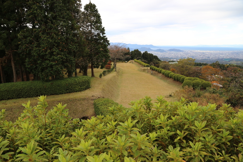 <p>【山中城】岱崎出丸・御馬場曲輪の一段高い平場から南西を撮影。 突き当りがすり鉢曲輪で、一段低くなっている。写真では見えないが、岱崎出丸の南西側には畝堀がある。 岱崎出丸は想像よりも広かった。</p><br><p>右下に箱根旧街道が通っていて、そこから豊臣軍が寄せてきた。岱崎出丸の守将は間宮康俊だったとのこと。北条守備兵は右側の土塁から鉄砲を浴びせていたのだろう。</p><br><p>右上には駿河湾と市街地（三島・沼津）が見える。 駿河湾と市街地の間に、丘陵がある。右から２番目の山が香貫緑地で、その手前に戸倉城がある。</p>