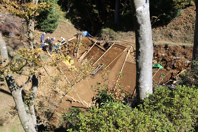 【山中城】元西櫓から復元中の空堀を撮影。<br>      人のサイズで、空堀の規模が分かる。<br><br>      復元作業を見ていたら、空堀上の線路に、土のカゴを6個くらい載せたトロッコが行き来していた。現代の技術をもってしても、なかなか骨が折れそうな様子だった。<br><br>      この写真には写っていないが、畝堀の底にハシゴが置いてあることもあった。下に降りると、ハシゴがないと登れないのだと思う。<br>      関東の山城に行くと、ロープをつたって斜面を登ることがあるが、地面が濡れていると、激しく滑る。<br>      ただ、これは道具なしで登った場合の話で、攻城兵も滑りやすい斜面や畝堀に落ちた時の脱出道具などを持っていたのではないだろうか。この辺の工夫の解説は読んだことがない。興味深いところだ。