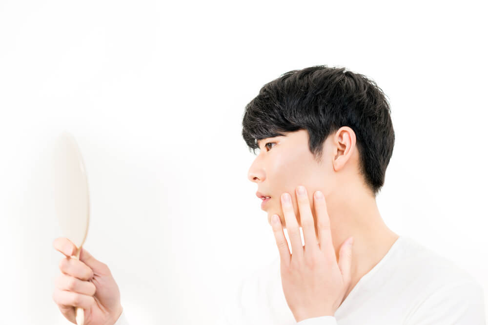 鏡を見ながら頬に手を当てる男性