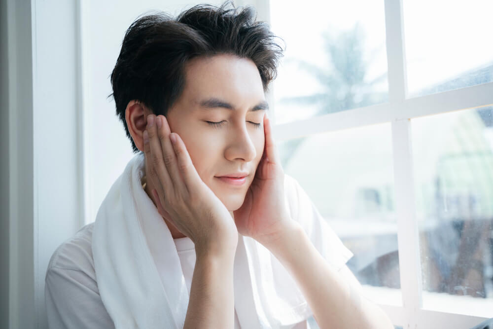 窓際で頬に両手を当てる男性