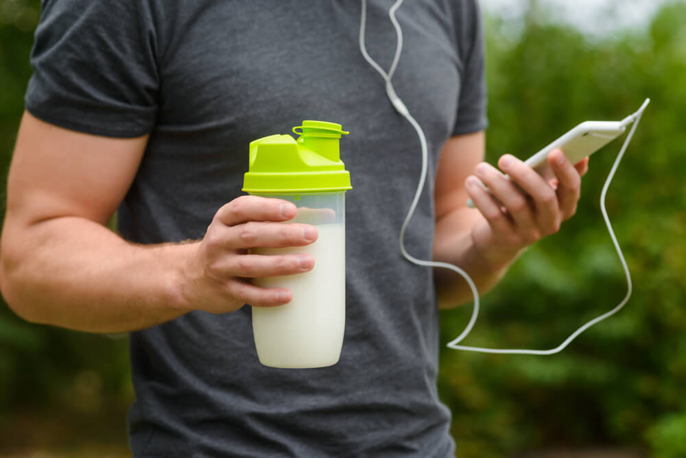 スマホを見ながらプロテインを飲む男性