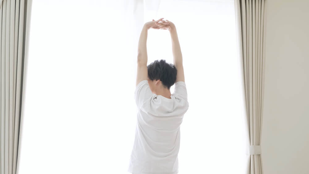 窓際で背伸びをする男性