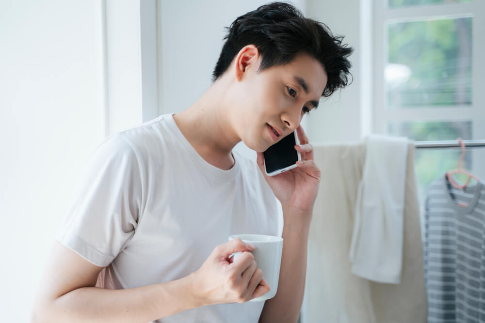 コーヒーを飲みながら携帯で話す男性