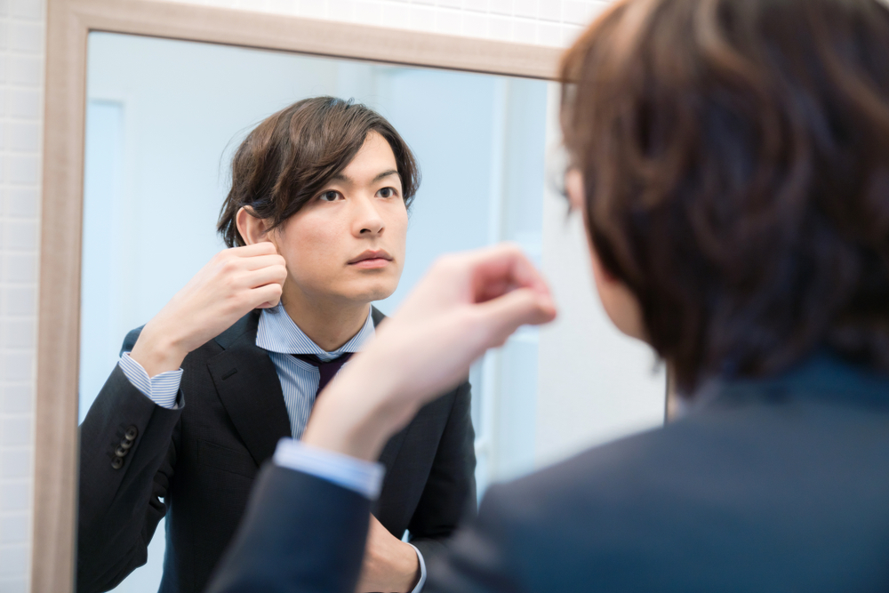 鏡を見ながら髪をいじる男性