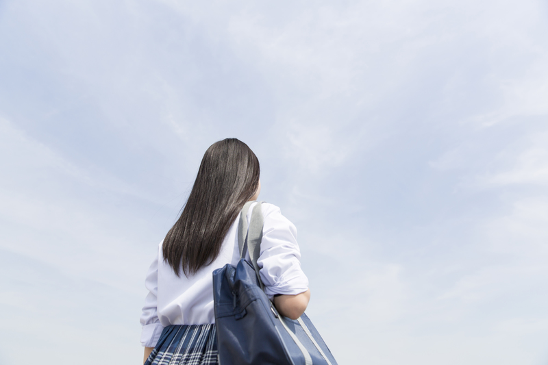 一人で立って歩く背中の高校生くらいの子ども