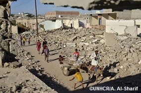 ジンジバルのアルオラ近郊で破壊された建物の間をろばの荷馬車が通る横で遊ぶ子どもたち。