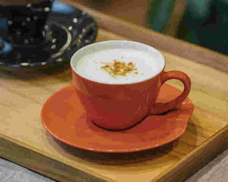 オレンジーのティーカップにきな粉を入れた豆乳コーヒーが注がれている