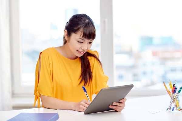 タブレットを見ながらメモを取る女性