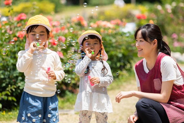 シャボン玉で遊ぶ女の子と保育士の写真