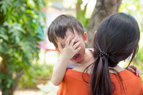泣く子どもを抱えて去る保育士の写真