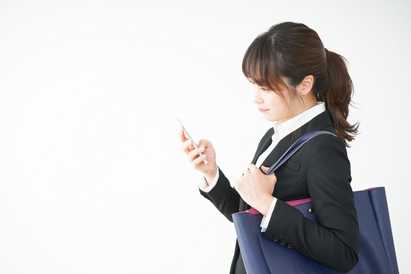 就活バッグを持って携帯をさわる女性
