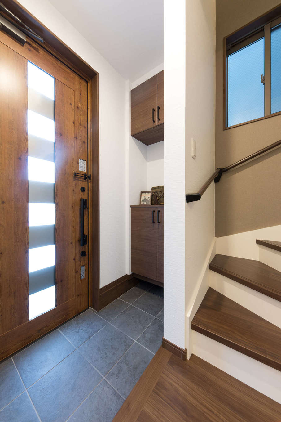 玄関はホールをなくしてスペースを節約 たたきの石板タイルが室内のヴィンテージインテリアと調和している 玄関ドアは採光ができるタイプにして閉塞