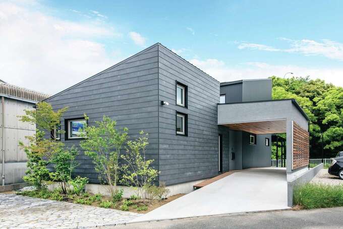 屋根付きのエントランスがある角張ったフォルムがクールな外観 濃いグレーのガルバリウム鋼板で外壁を統一し ガレージの天井を板張りにしてアクセン