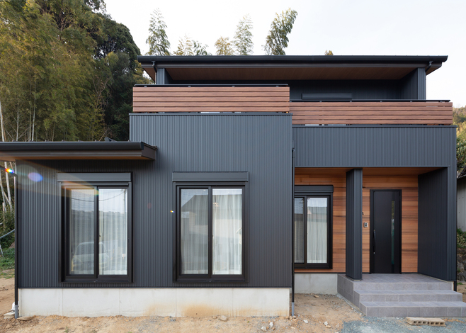 建物のすぐ裏手に山がある立地を配慮し 外壁には苔の付着を防ぐ効果と耐久性に優れたガルバリウム鋼板を採用 玄関周りの壁はレッドシダーの板張りに