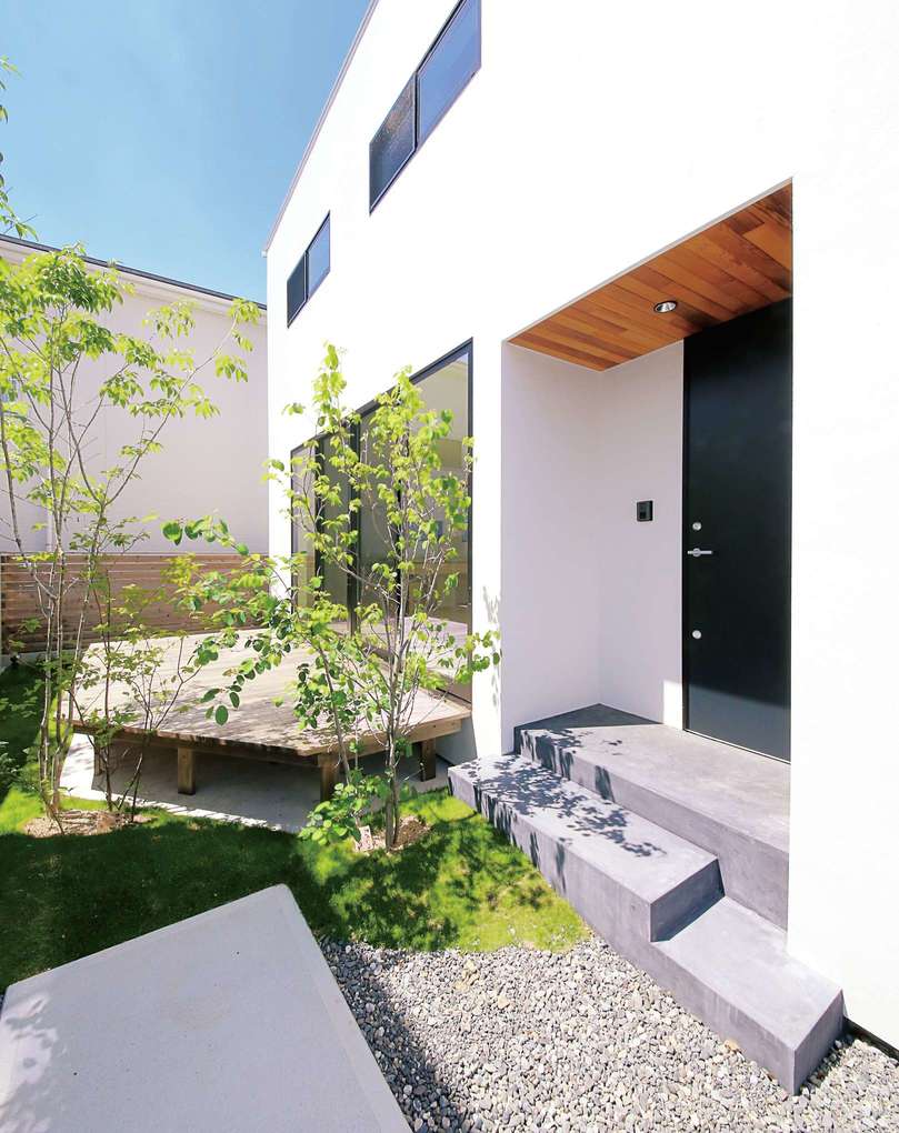 建物の東側に設けたアプローチを進むと 横長の玄関ポーチがある その奥には庭と広いデッキが見える イエタテ