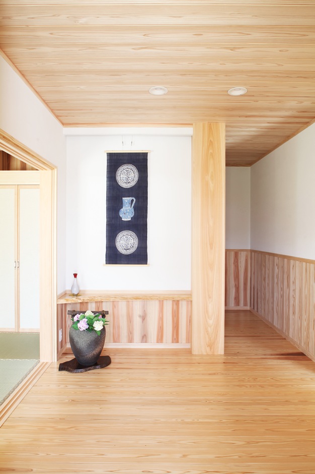 広々とした玄関で家族やゲストを出迎えるのは35cm角のヒノキの大黒柱 正面の壁は腰板を低くして白壁の面積を広くとり タペストリーや絵画を飾れ