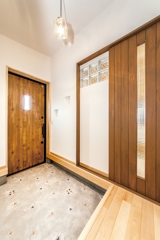 引き戸のチェッカーガラスやガラスブロックから リビングの明かりが届く 玄関ホールと そこから続くポーチにはカラフルなタイルをはめ込んだ イエ