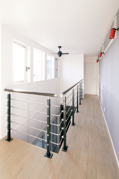 階段と2階ホールを金属の手すりにしたことで 吹き抜けの開放感がアップ モノトーンのシックな空間にご主人が選んだ真紅のソファが映えるスタイリッ