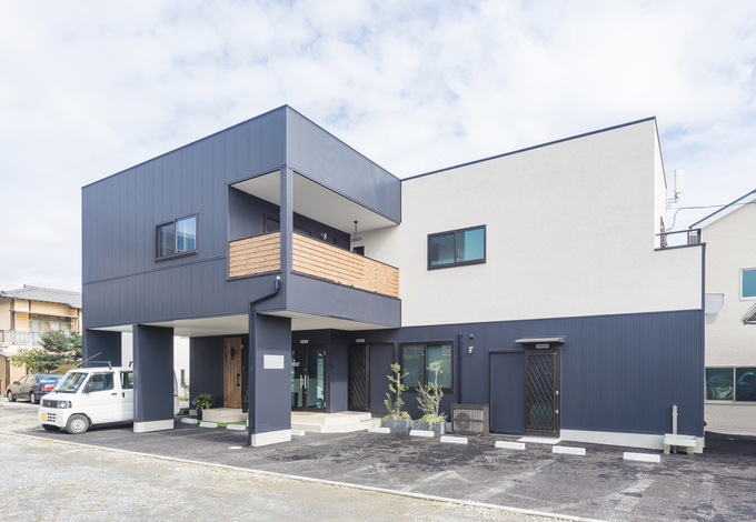 ガルバリウム鋼板と塗り壁の異素材の組み合わせがモダンな印象の外観 バルコニーの木調の壁もアクセントに 事務所の入り口の脇に住宅用の玄関を設け