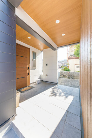 広々としたピロティタイプの玄関ポーチは 雨の日の出入りも苦にならない 木質の軒天井で温かみをプラス イエタテ