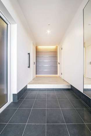 白 黒 グレーでまとめた玄関 左手の入り口はビルトインガレージに続いている 正面のグレーの壁にはスチールのラインを入れてクールに演出 イエタ