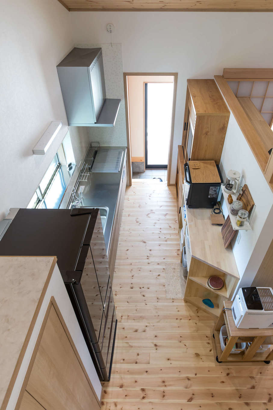 ロフト部分からキッチンを見おろす 壁で閉じられていないので開放感がある 奥には土間に通じる開口部が 冷蔵庫の手前にはクローゼットタイプのパン