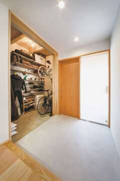 玄関とリビングをつなぐ細長い土間が建物の奥行き感を強調 自転車置き場など多目的に使えるので便利 壁代わりの収納には家族分の靴がたっぷり収まる