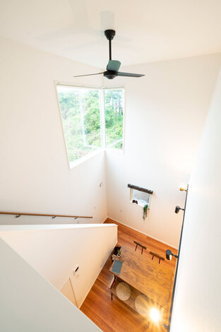 白い壁と天井が織りなす吹き抜け空間に 高窓から見える緑が鮮やかに映える ２階にいても吹き抜けを通じて常に家族の気配を感じとれる イエタテ