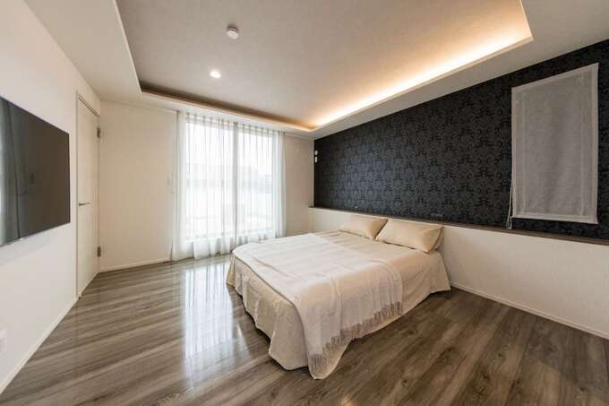 アクセントクロスと折上天井の間接照明でムーディに演出した主寝室 掃出窓の外にはバルコニーがある イエタテ