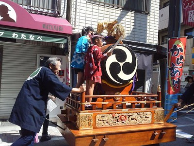 戸越銀座の商店街にある山車を押す大人と太鼓を叩く子どもたちの画像