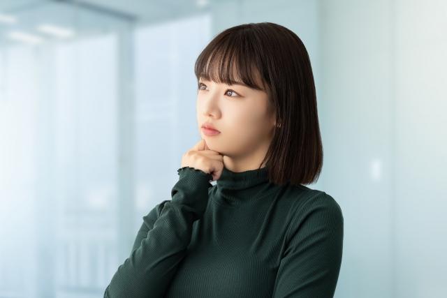 静かな室内で顎に手を当てて考え込む女性の横顔。性自認の揺れや自分の気持ちを見つめるイメージ写真