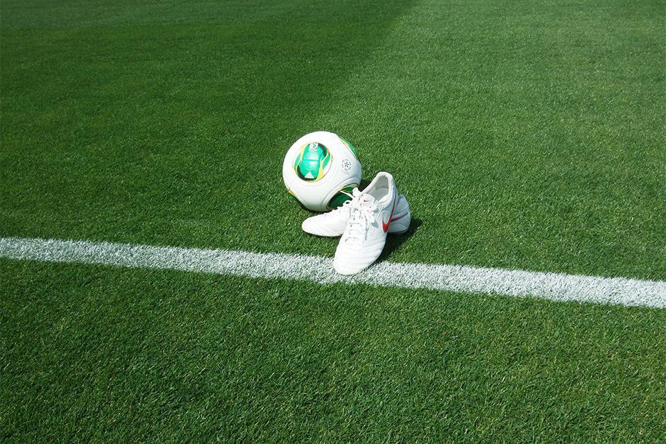 芝生のサッカーグラウンドに置かれたボールとスパイクの写真。教え子たちとの思い出や、サッカー指導の象徴として第2部の内容を表すイメージ。