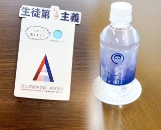 校長の似顔絵がデザインされたミネラルウォーターやメモ用紙