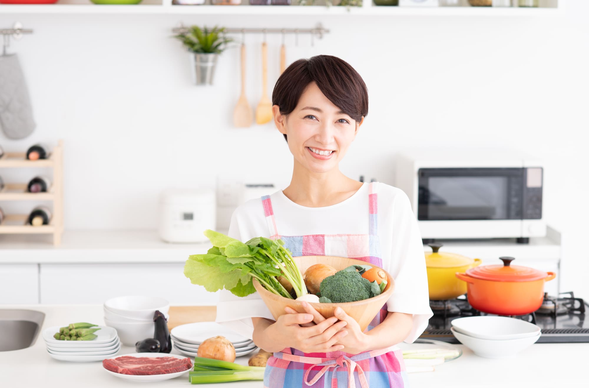 野菜が入った木のボウルを手に持ったエプロン姿の女性