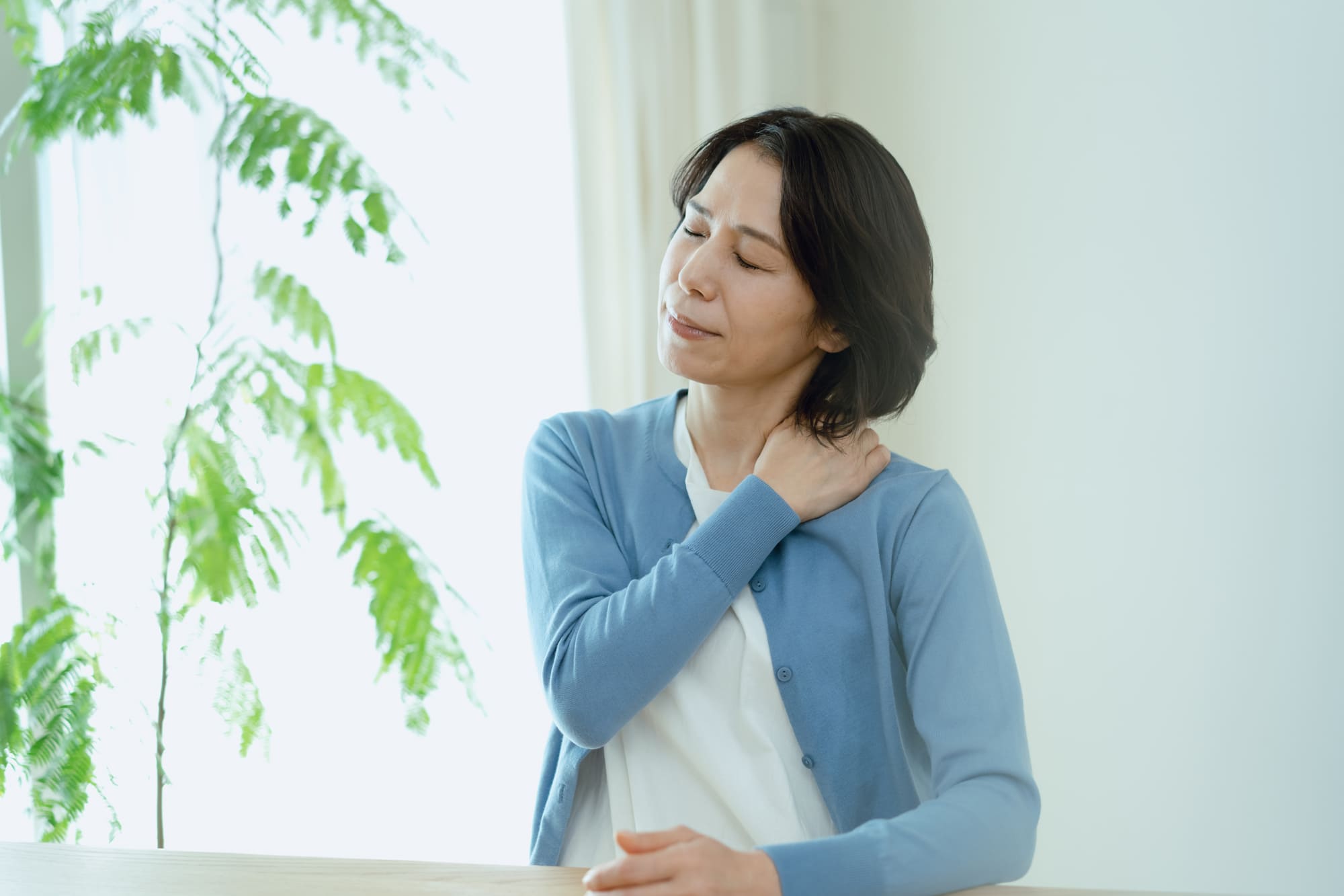 片手で肩を押さえて疲れた表情を浮かべる女性