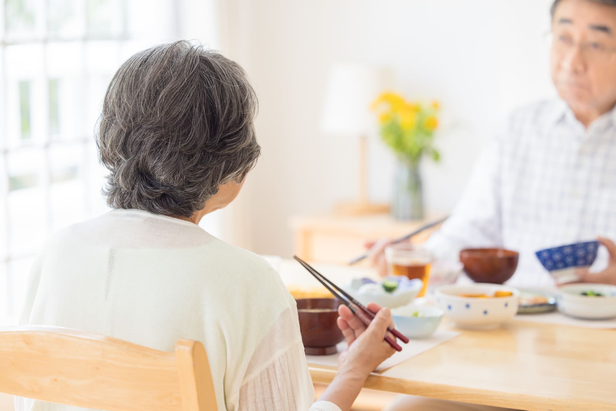 テーブルで向かい合って食事をするシニア夫婦