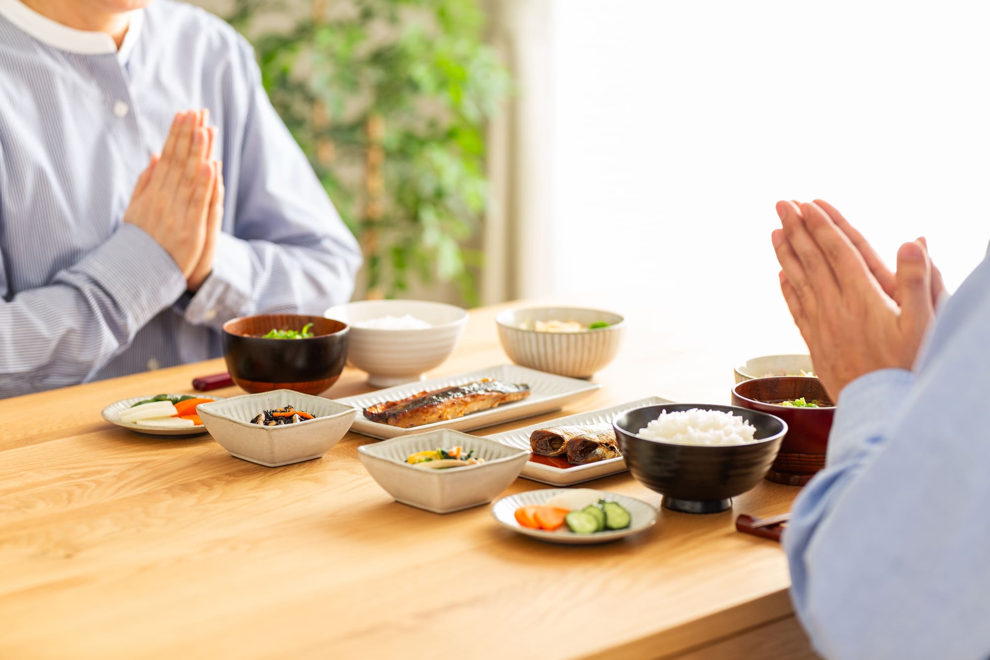 和食が並ぶ食卓で手を合わせる夫婦
