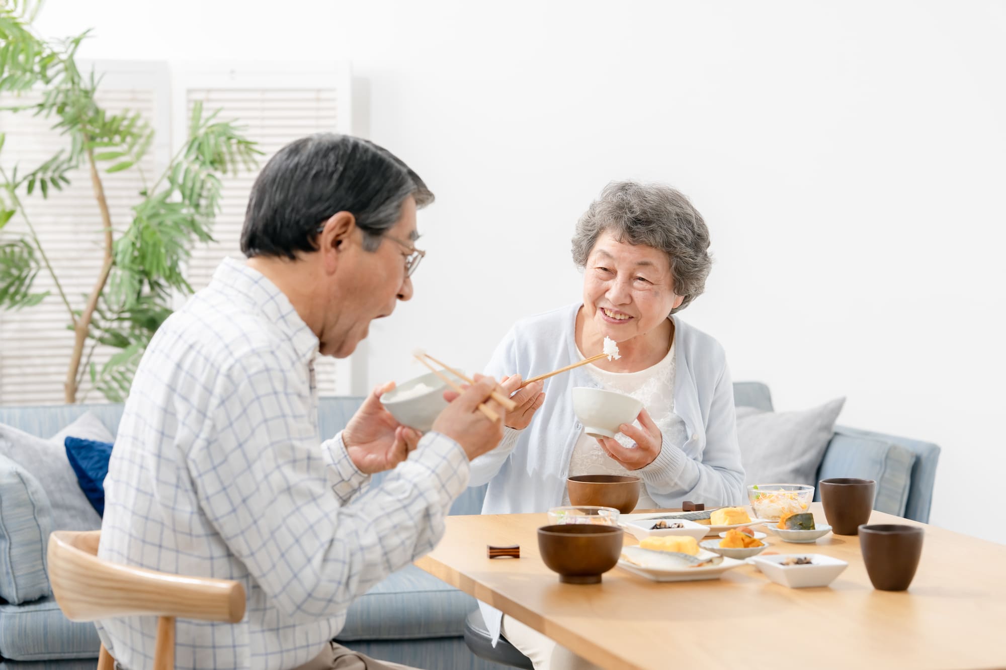 テーブルで向かい合い、笑顔で食事をするシニア夫婦