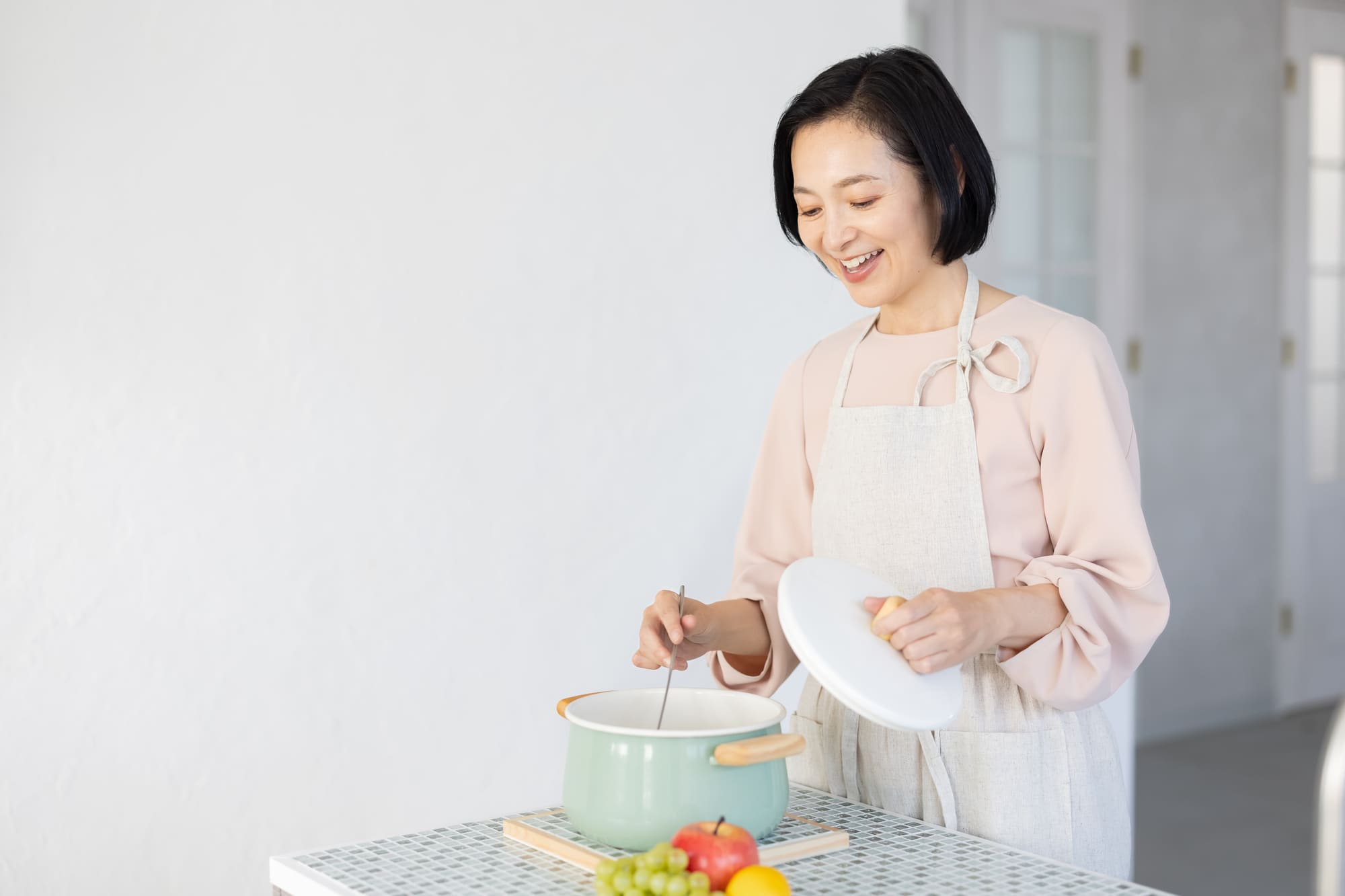 キッチンに立ち、鍋をお玉でかき混ぜる女性