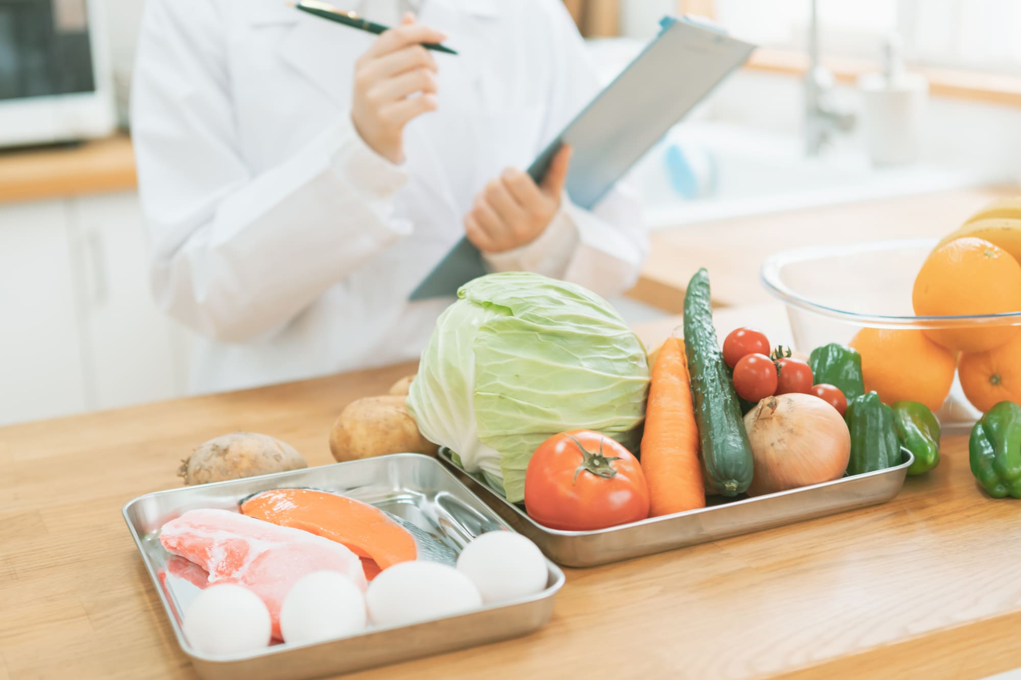 たくさん並んだ肉や野菜などの食材とバインダーを持つ白衣の人物