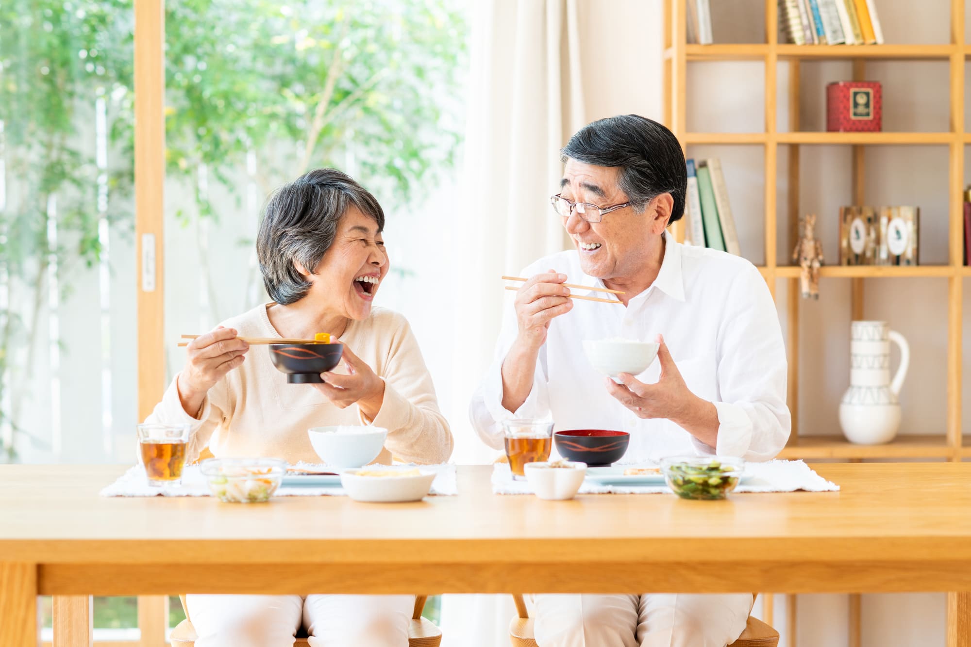 テーブルに並んで座り、笑顔で食事を楽しむシニア夫婦