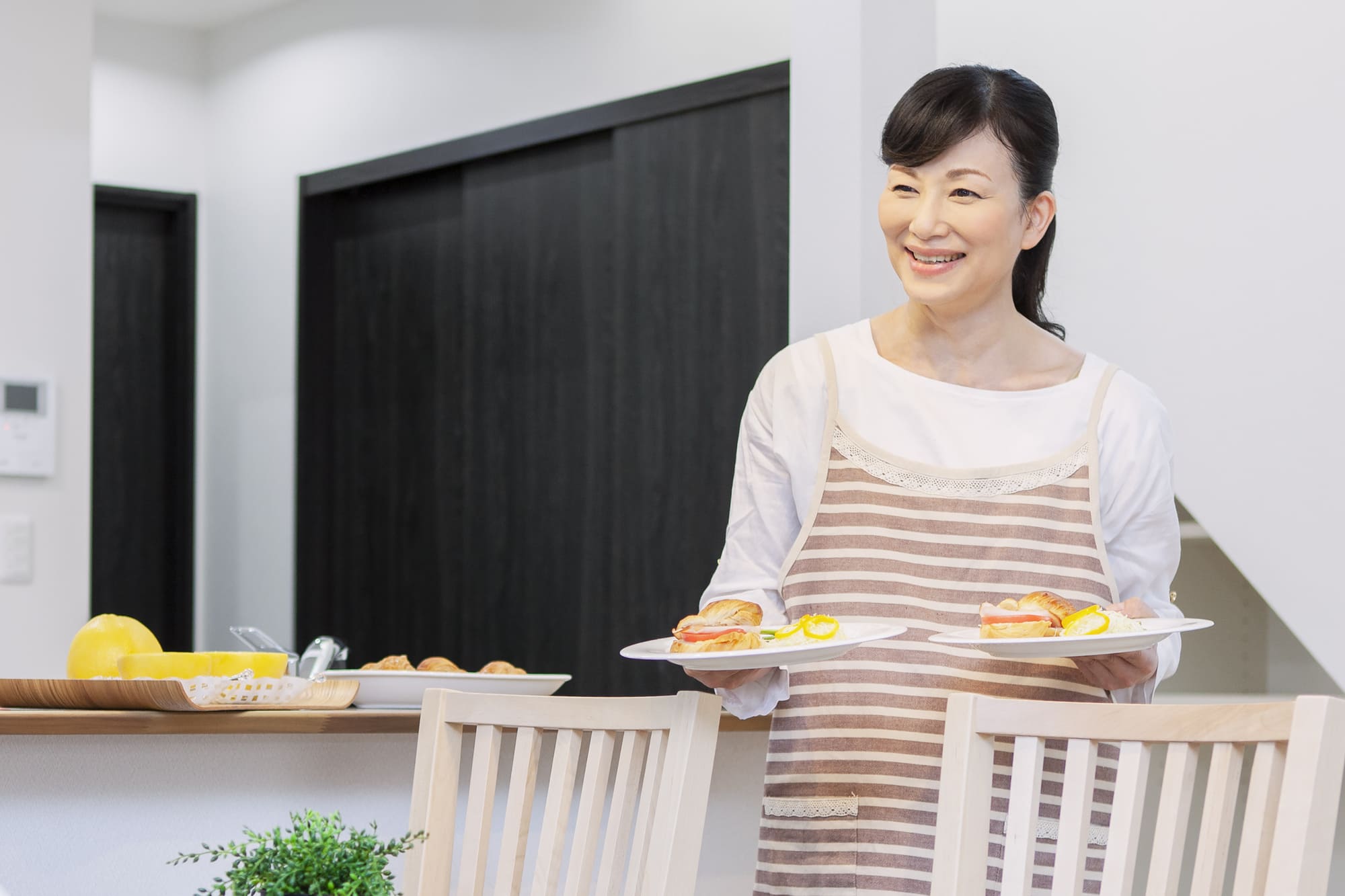 食卓に料理を運んでいるエプロン姿の女性