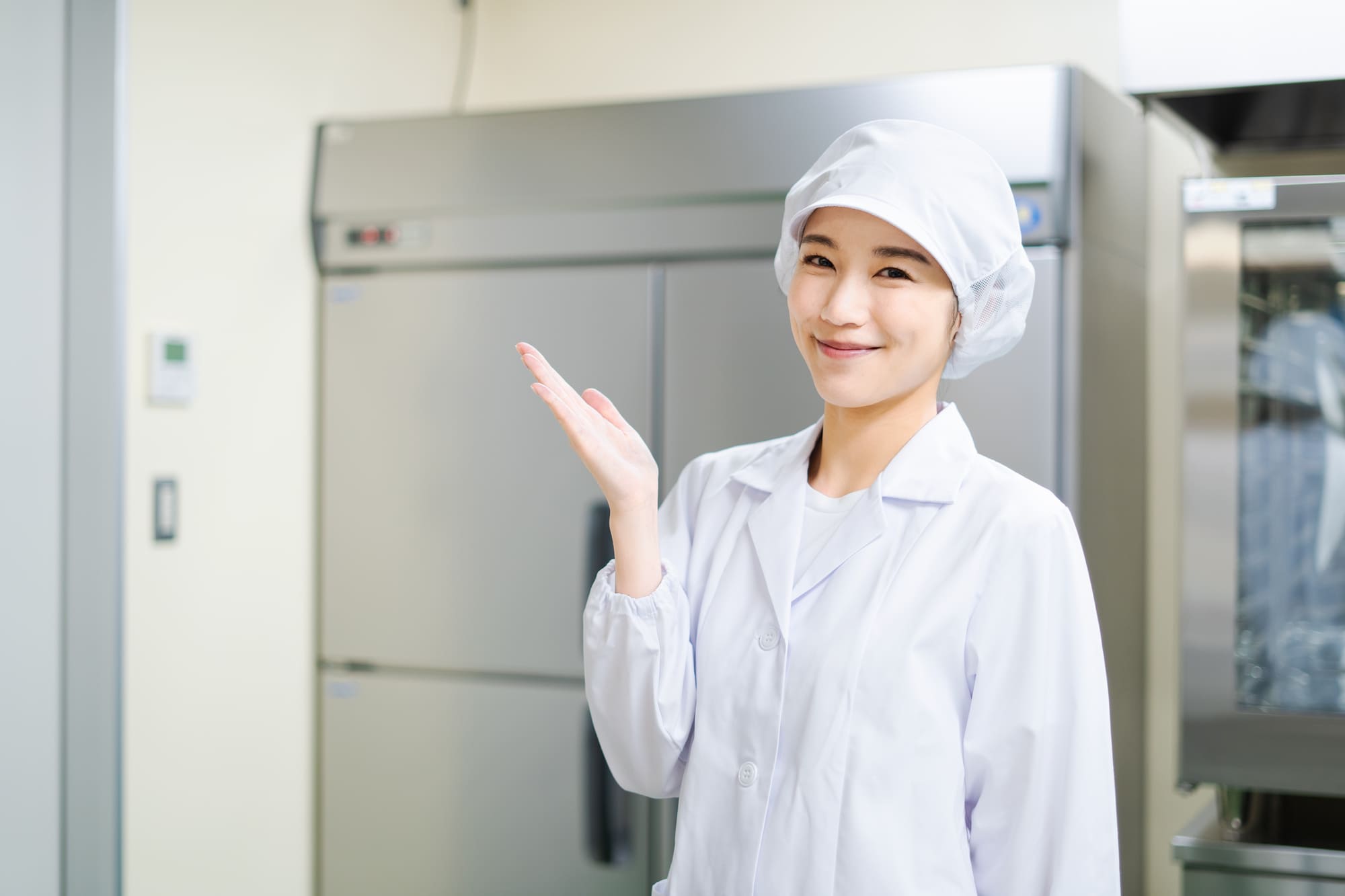 手のひらを上に向けて笑顔を浮かべる女性調理師