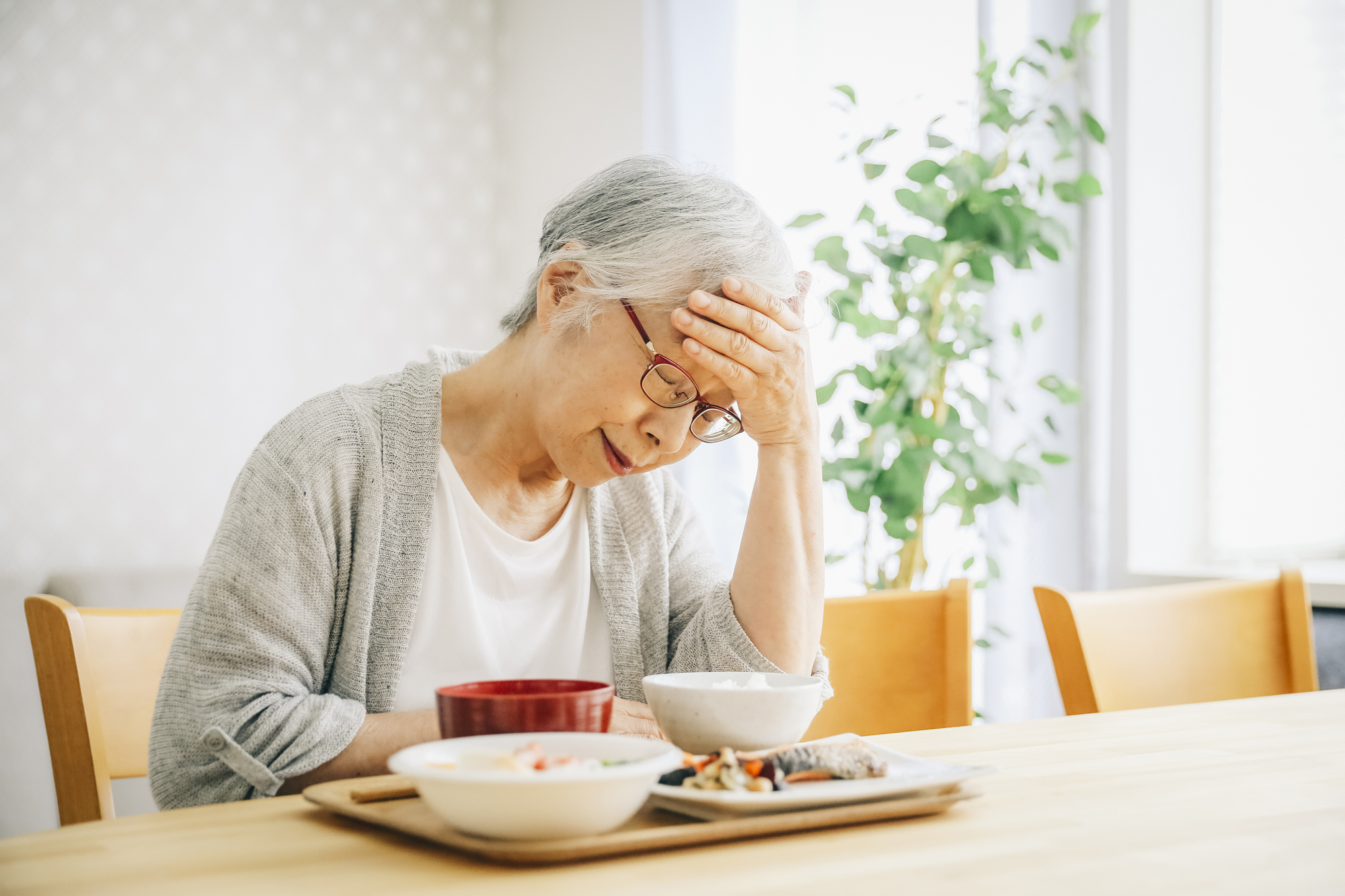 机に置かれた食事と頭を抱える女性